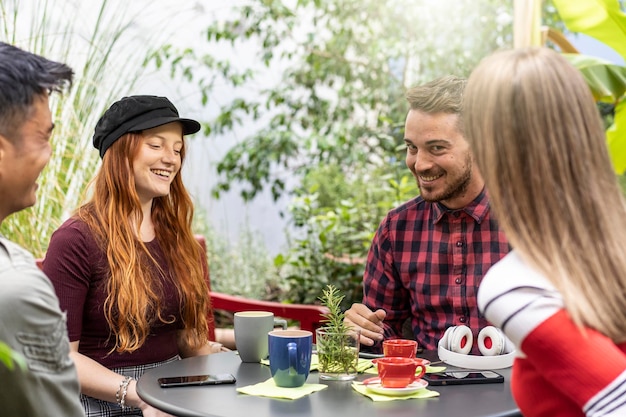 コーヒーバーガーデンでラテを飲む人々のグループ ホステルデホールで話し、一緒に楽しんでいる幸せな友達 オープンエアのカフェで幸せな男と女とのライフスタイルコンセプト 暖かい鮮やかなフィルター