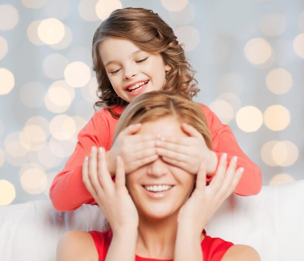 people, happiness, leisure, family and motherhood concept - happy mother and daughter playing guess who game over holidays lights background