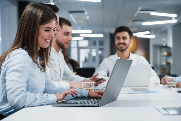 People have business conversation Side view of girl works on the silver colored laptop in the office and smiling