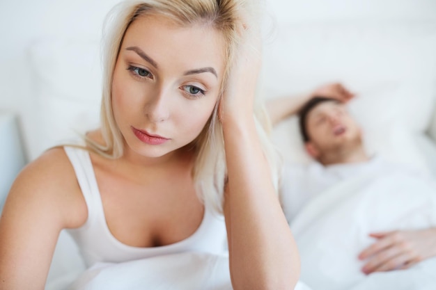 人、健康、睡眠障害のコンセプト – 家のベッドにいる夫婦、いびきをかく男性、不眠症に苦しむ若い女性