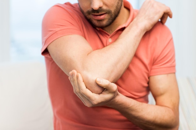 People, healthcare and problem concept - close up of man suffering from pain in hand or elbow at home