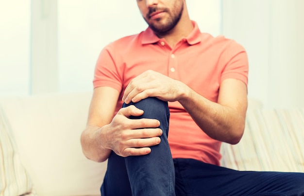 people, healthcare and problem concept - close up of young man suffering from pain in leg or knee at home