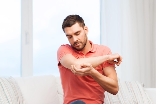 people, healthcare and problem concept - unhappy man suffering from pain in hand at home