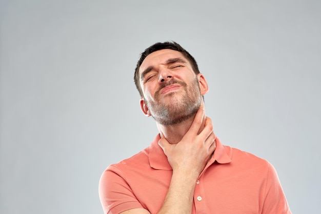 people, healthcare and problem concept - unhappy man touching his neck and suffering from throat pain over gray background