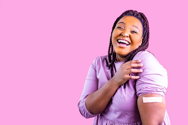 People healthcare and protection concept positive woman getting vaccination and showing a hand with plaster in pink studio