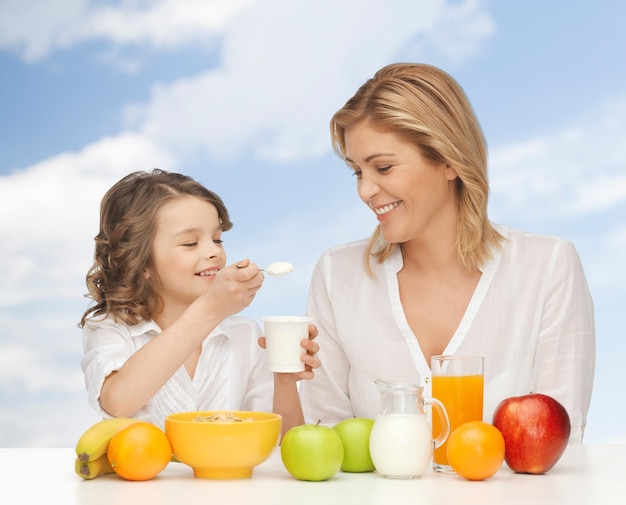 people, healthy lifestyle, family and food concept - happy mother and daughter eating healthy breakfast over blue sky background