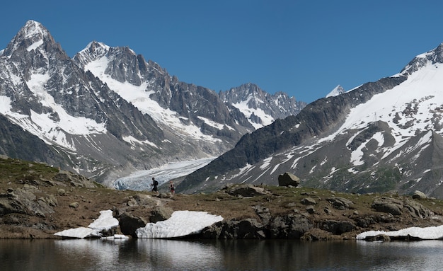 People hiking and doing trekking by a lake in the mountains with glacier