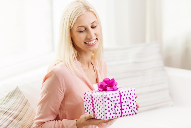 人、祝日、お祝い、誕生日のコンセプト – 家にギフトボックスを持つ笑顔の若い女性
