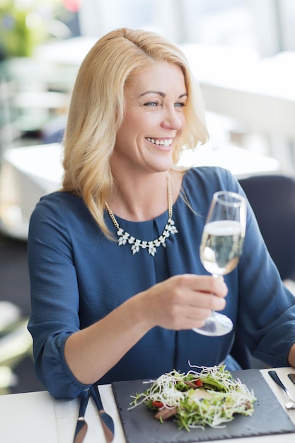 人、休日、ライフスタイルのコンセプト – レストランでシャンパンを飲む幸せな笑顔の女性