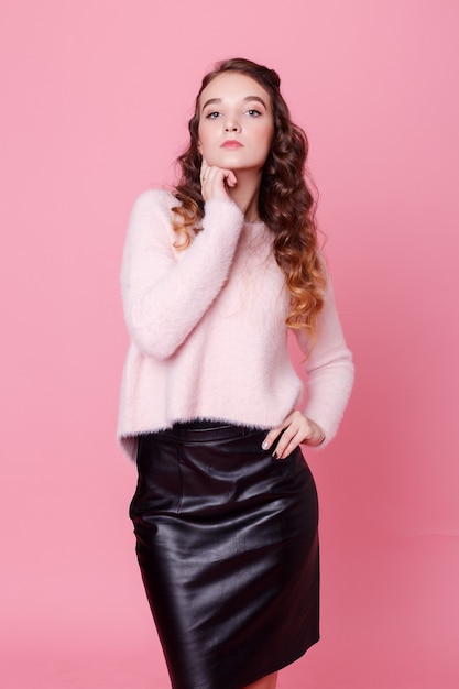 People, holidays, luxury concept - Smiling beautiful young woman in a black leather skirt presenting something and looking at camera. studio shot pink background. Portrait of a pretty teenager girl