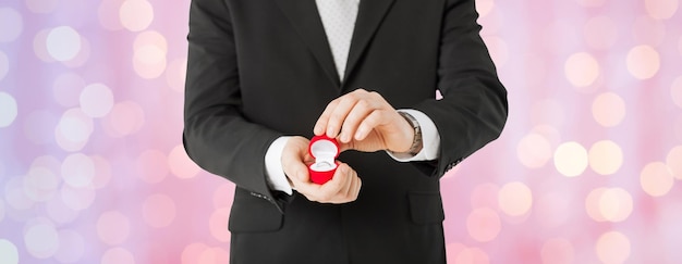人、休日、プレゼント、提案のコンセプト – ホリデーライトの背景にギフトボックスと婚約指輪を持つ男性の接写