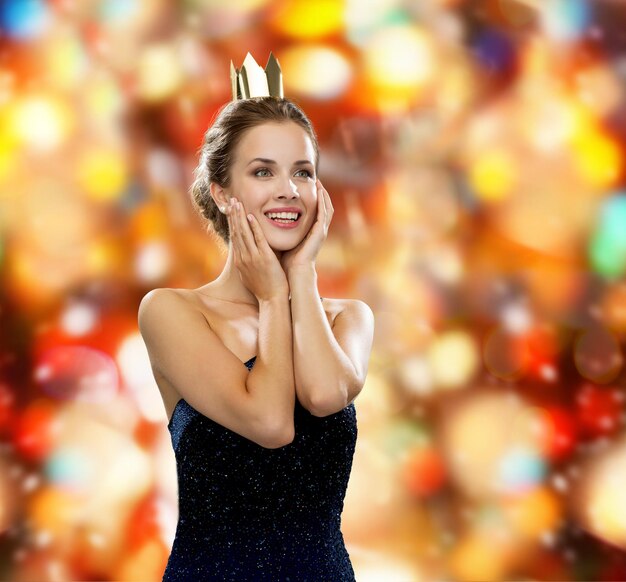 люди, праздники, роялти и гламурная концепция - улыбающаяся женщина в вечернем платье с золотой короной на фоне красных огней