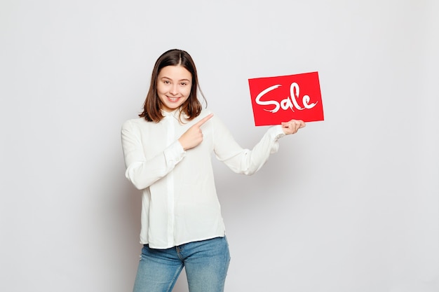 People, holidays, sale, shopping and advertisement concept - Young smiling brunette girl is holding a sale sign