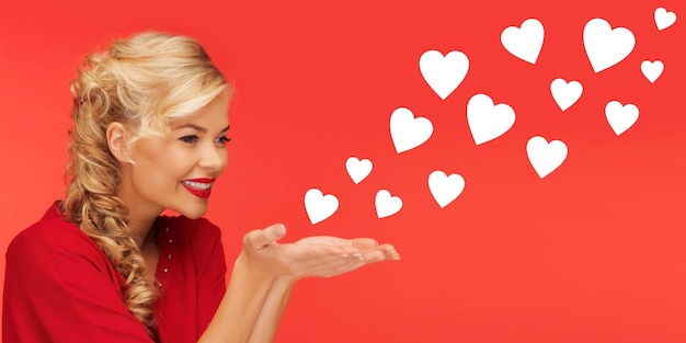 people, holidays, valentines day and love concept - lovely woman in red clothes sending heart shapes from on palms of her hands over red background