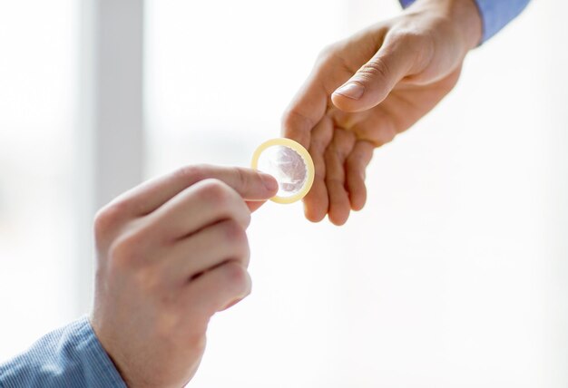 people, homosexuality, safe sex, sexual education and charity concept - close up of happy male gay couple hands giving condom