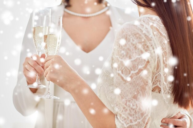 people, homosexuality, same-sex marriage, celebration and love concept - close up of happy married lesbian couple holding and clinking champagne glasses over snow effect