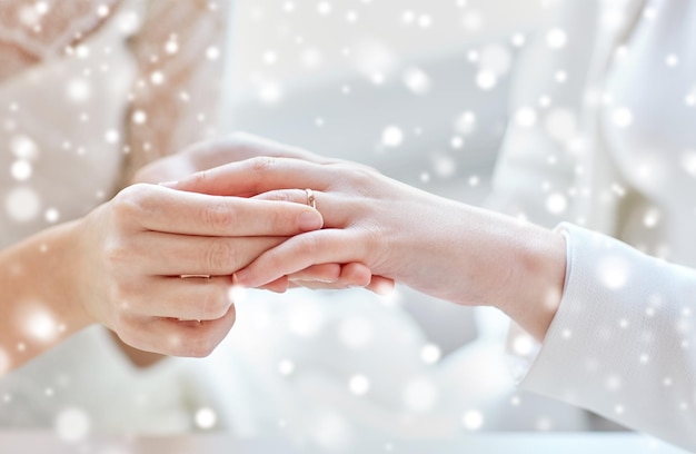 人、同性愛、同性結婚、愛のコンセプト – 雪の効果の上に結婚指輪をはめた幸せなレズビアンの夫婦の手の接写