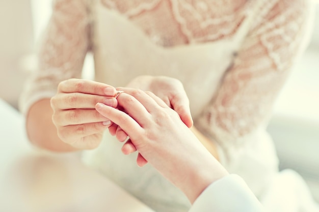 people, homosexuality, same-sex marriage and love concept - close up of happy lesbian couple hands putting on wedding ring