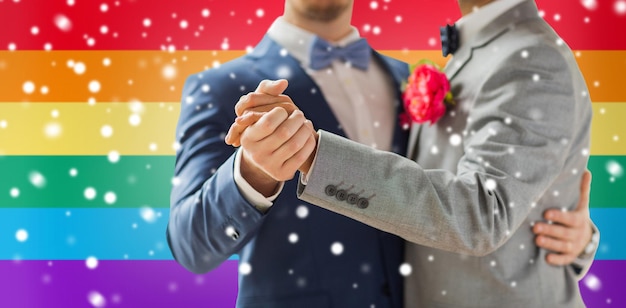 люди, гомосексуальность, однополые браки и концепция любви - крупный план счастливой мужской гей-пары, держащейся за руки и танцующей на свадьбе на фоне радужного флага и эффекта снега