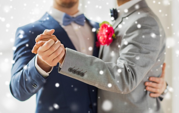 people, homosexuality, same-sex marriage and love concept - close up of happy male gay couple holding hands and dancing on wedding over snow effect