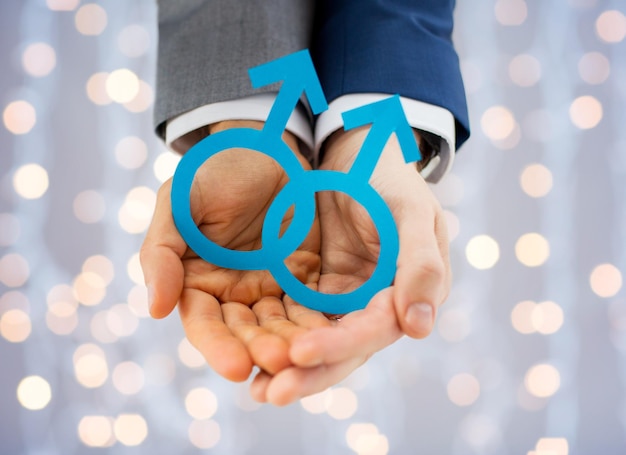 people, homosexuality, same-sex marriage and love concept - close up of happy male gay couple holding paper cutout love symbol over holidays lights background