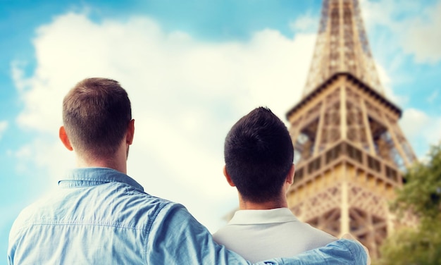 people, homosexuality, same-sex marriage, travel and love concept - close up of happy male gay couple hugging from back over paris eiffel tower background