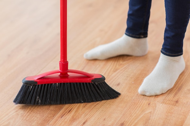 Concetto di persone, lavori domestici, pulizia e pulizia - primo piano delle gambe della donna con il pavimento della scopa a casa