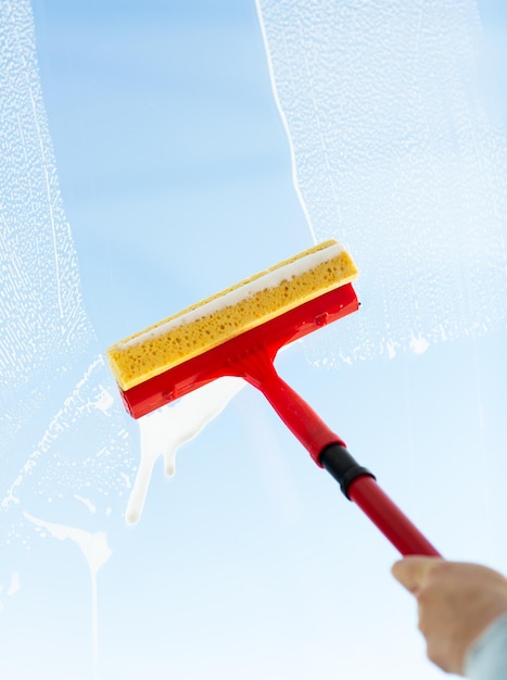 people, housework and housekeeping concept -close up of hand cleaning window glass with sponge mop and foam