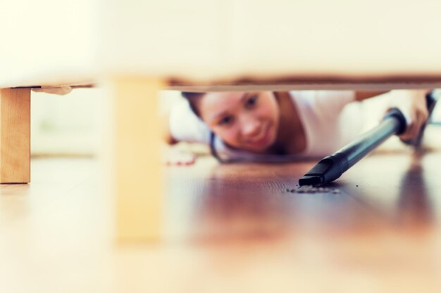 Foto concetto di persone, lavori domestici e pulizie - primo piano di una donna felice con un aspirapolvere che pulisce il pavimento sotto il divano a casa