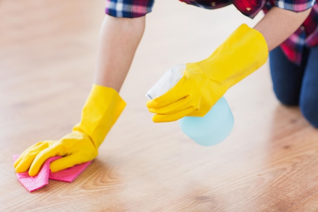 Concetto di persone, lavori domestici e pulizie - primo piano di donna in guanti di gomma con panno e spray detergente per pulire il pavimento a casa