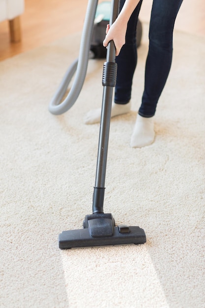 people, housework and housekeeping concept - close up of woman with legs vacuum cleaner cleaning carpet at home