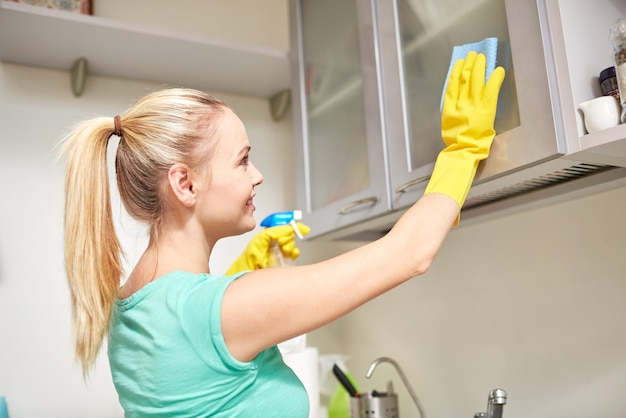 Concetto di persone, lavori domestici e pulizie - armadio per la pulizia della donna felice con straccio e detergente nella cucina di casa