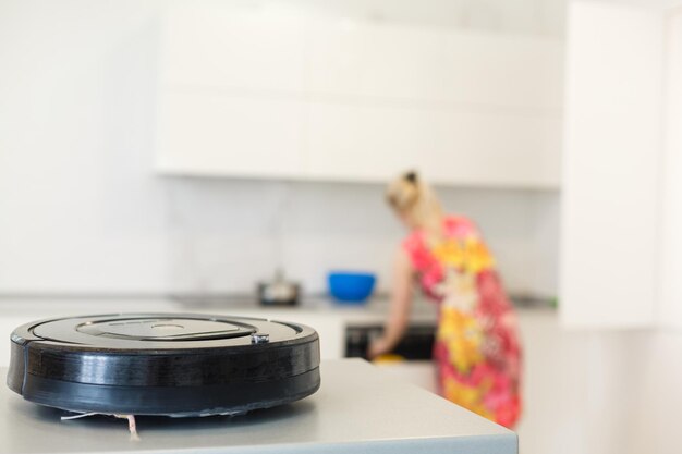 People, housework and technology concept - happy woman and\
robot vacuum cleaner