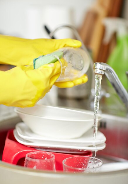 人、家事、洗濯、ハウスキーピングのコンセプト-家庭の台所でスポンジで皿を洗う保護手袋をはめた女性の手のクローズアップ