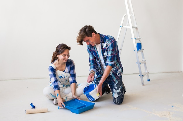 People and interiors concept - Young couple sitting on the white floor and pour paint