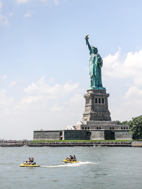 people jet skiing in sea by statue of liberty against sky