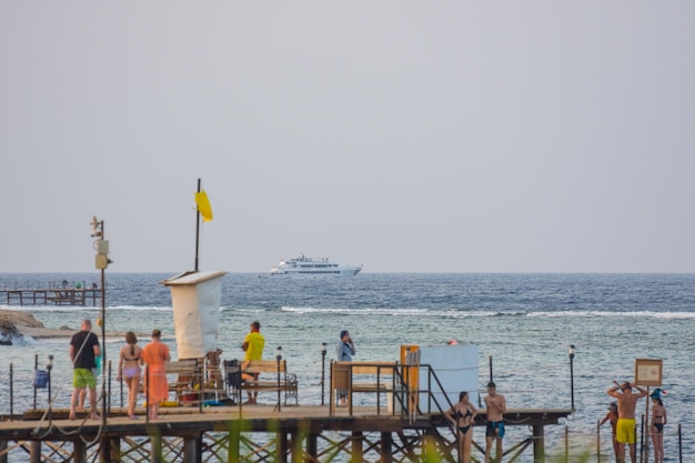 People on a jetty and a yacht at the horizon