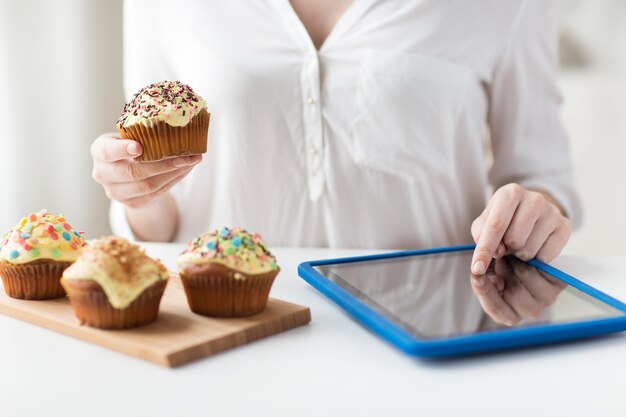 Foto persone, cibo spazzatura, dieta, tecnologia e concetto di alimentazione malsana - primo piano di donna con cupcakes glassati o muffin e computer tablet pc che conta le calorie