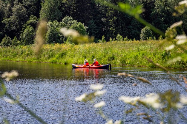 森を背景に川でカヤックをする人々。アクティブな夏のスポーツ。美しい風景。
