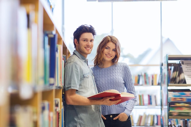 人、知識、教育、学校のコンセプト – 図書館に本を持つ幸せな学生夫婦