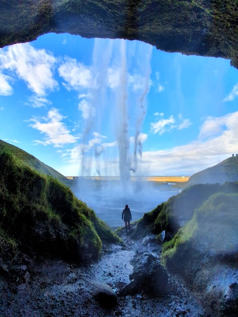 People on land against sky behind waterfall