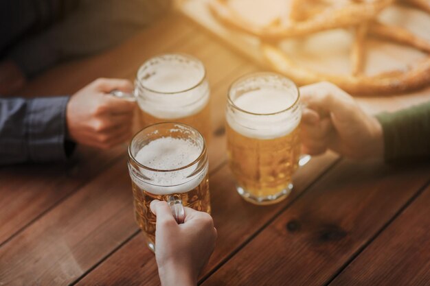 写真 人、レジャー、飲み物のコンセプト – バーやパブでビールジョッキを鳴らす男性の手の接写