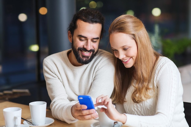 people, leisure, communication, eating and drinking concept - happy couple with smartphone drinking tea or coffee at cafe