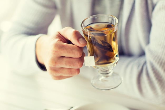 people, leisure and drinks concept - close up of man drinking tea at home or cafe