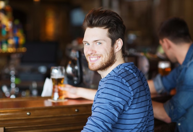 people, leisure and drinks concept - happy young man drinking beer at bar or pub