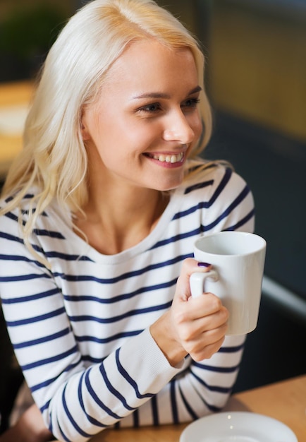 people, leisure, eating and drinking concept - happy young woman drinking tea or coffee at cafe or home