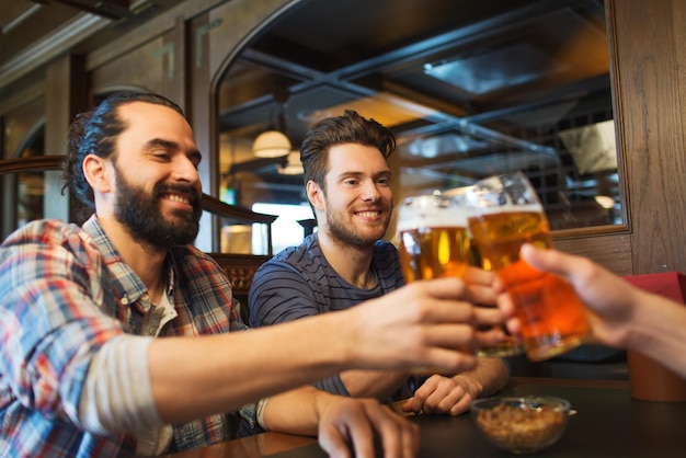 人、レジャー、友情、独身パーティー、お祝いのコンセプト – バーやパブでビールを飲み、グラスを鳴らす幸せな男性の友達