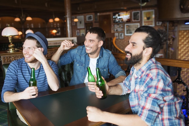 Concetto di persone, tempo libero, amicizia e addio al celibato - amici maschi felici che bevono birra in bottiglia e mani alzate che fanno il tifo per la partita di calcio al bar o al pub