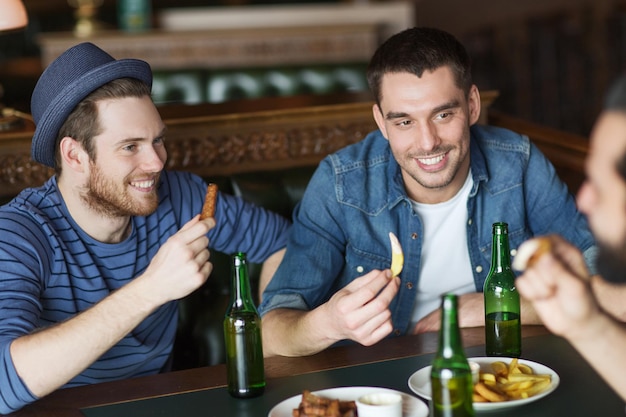 people, leisure, friendship and bachelor party concept - happy male friends drinking bottled beer and talking at bar or pub