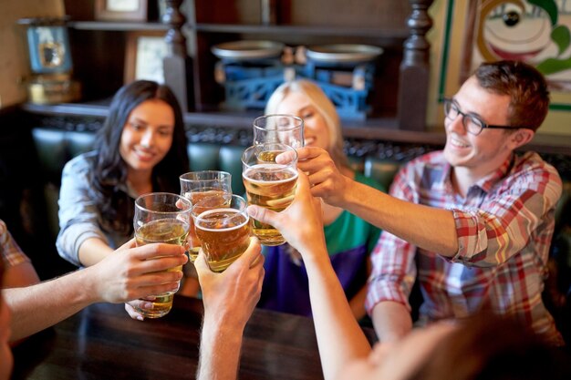 人、レジャー、友情、お祝いのコンセプト – バーやパブで生ビールを飲み、グラスを鳴らしている幸せな友達